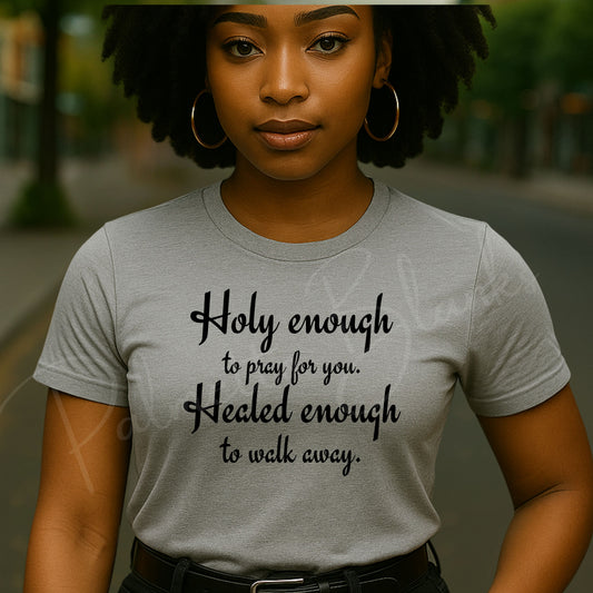 Woman wearing a light grey t-shirt with the phrase “Holy enough to pray for you. Healed enough to walk away” in bold black script – faith-based screen print transfer design.