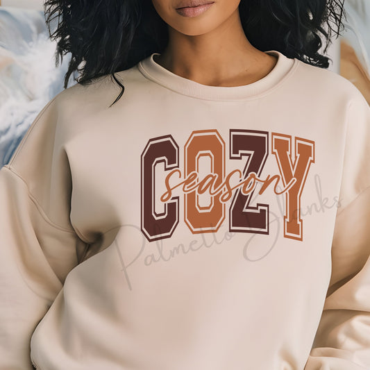 Beige sweatshirt featuring the “Cozy Season” design in bold varsity block letters with fall colors and script text overlay, ideal for screen print transfer apparel.