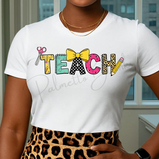 White t-shirt featuring the “TEACH” design with colorful school supply-themed letters including scissors, notebook, bow, leopard print, and pencil in a full color screen print style.